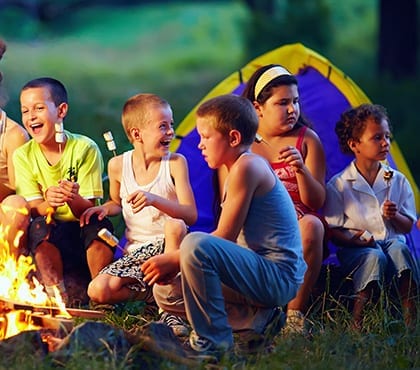 kids sitting around fire toasting marshmallows at camp that uses a managed service provider