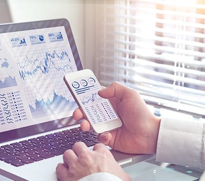 man looking at stats on a phone and laptop for company that uses managed service provider