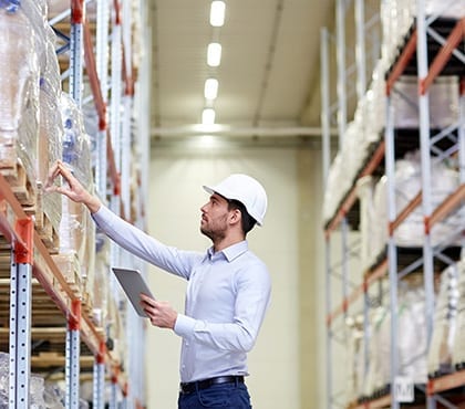 man wearing white hard hat checking inventory in warehouse for company that has it security